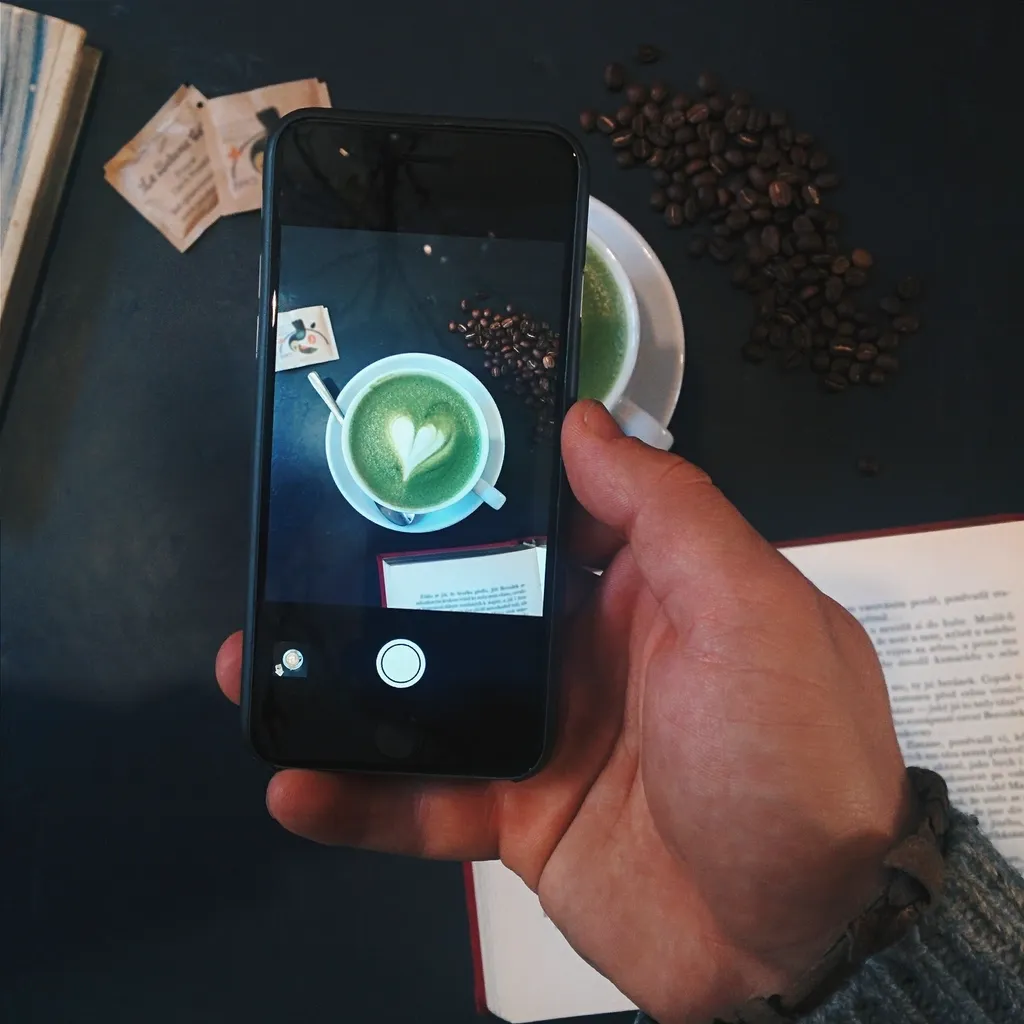 A hand photographing a matcha latte on a smartphone