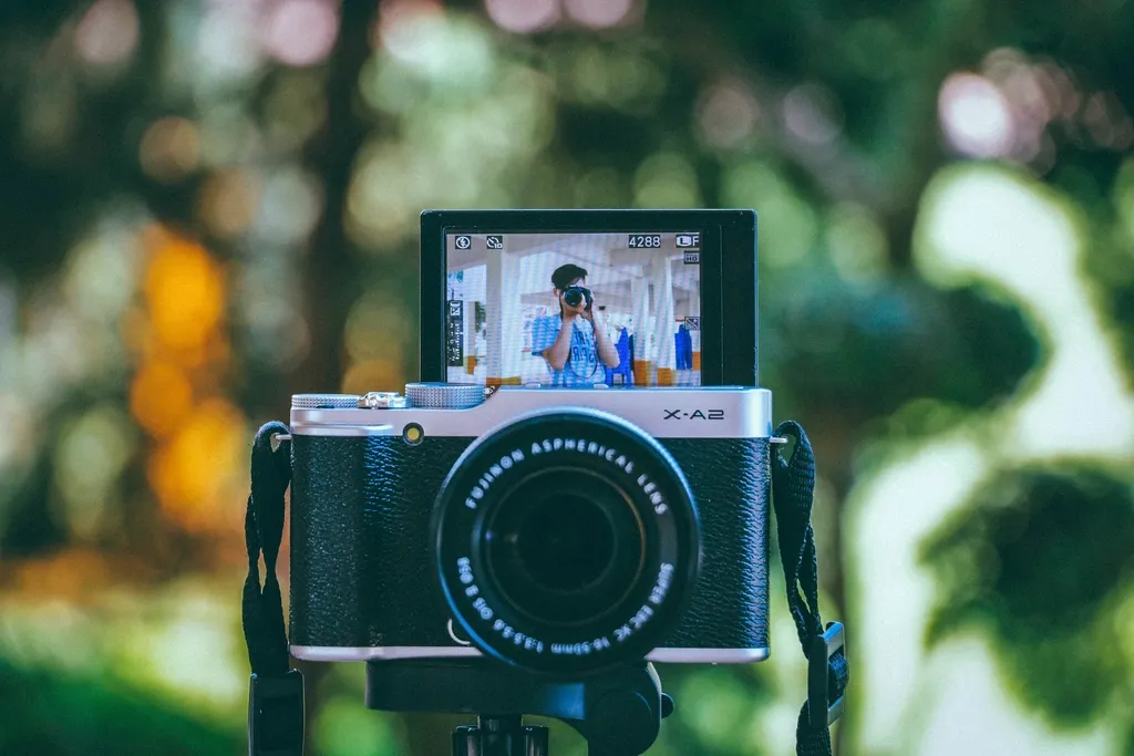 A mirrorless camera on a tripod, its flip screen showing a creator filming
